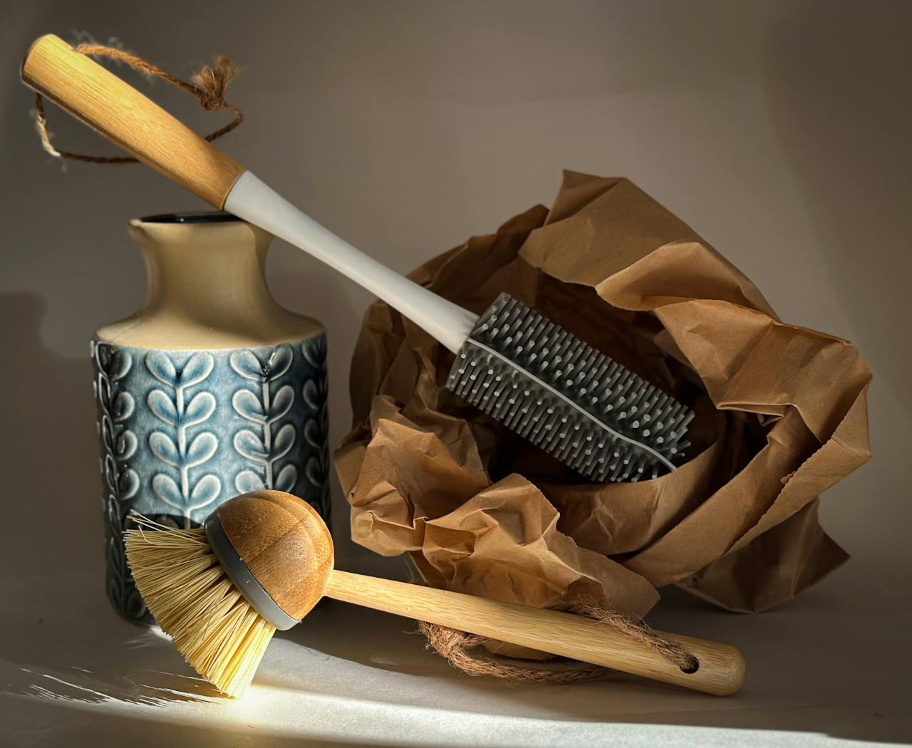 Stylish still life of eco-friendly cleaning brushes, a textured ceramic vase, and crumpled brown paper.